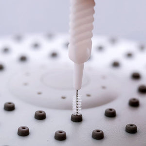 30Pcs Shower Nozzle Cleaning Brush with a white ribbed plastic handle and fine metal bristles cleaning a dark nozzle