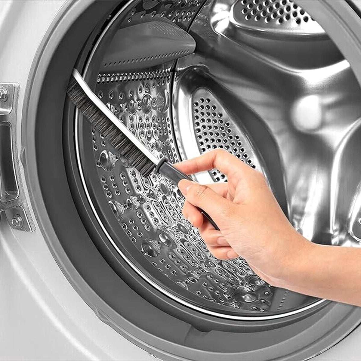 3x Hard-bristled Crevice Brush with a slim black handle and dark bristles cleaning a washing machine drum seam