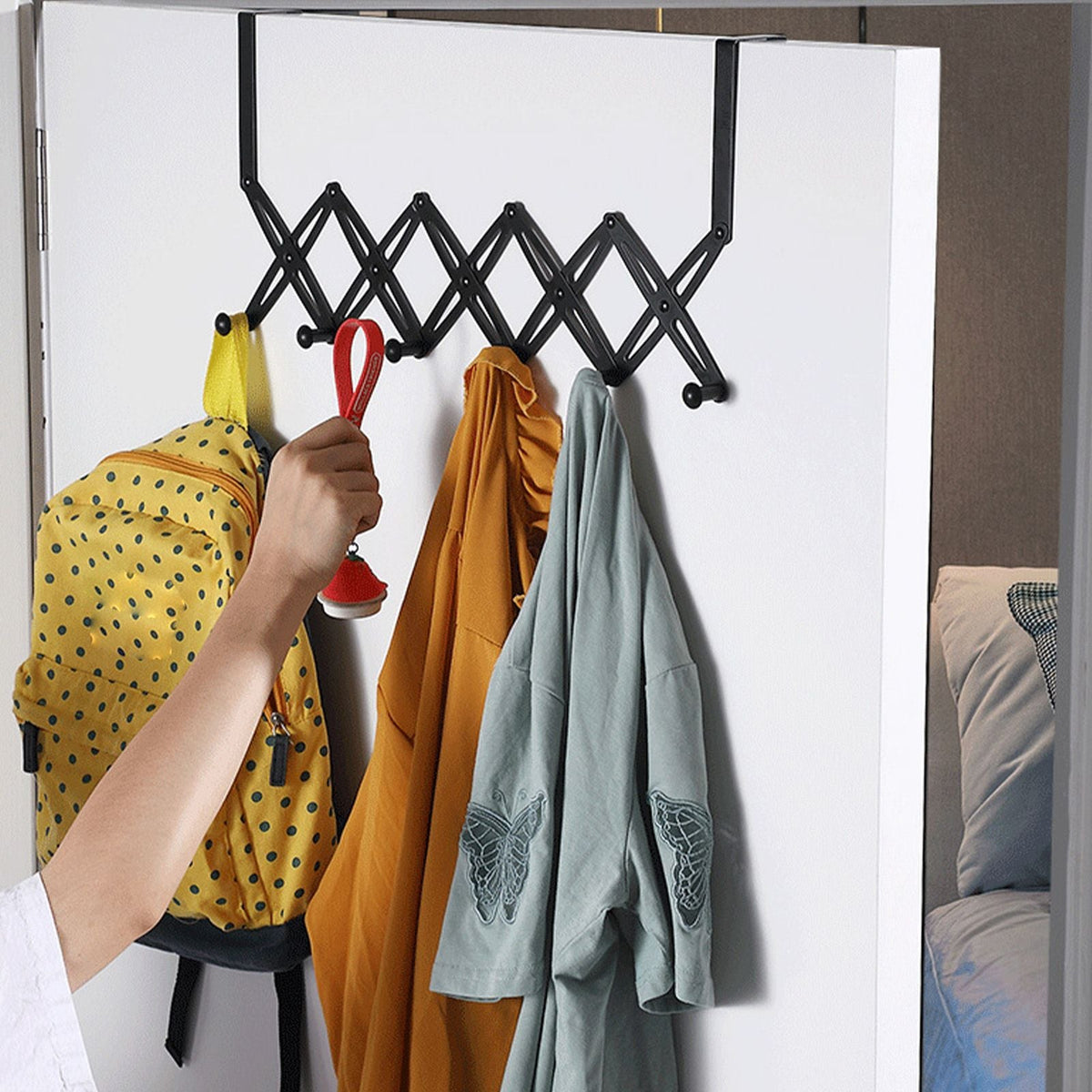 Over Door Hooks in black metal with an expandable accordion rack and multiple hooks holding clothing and a bag
