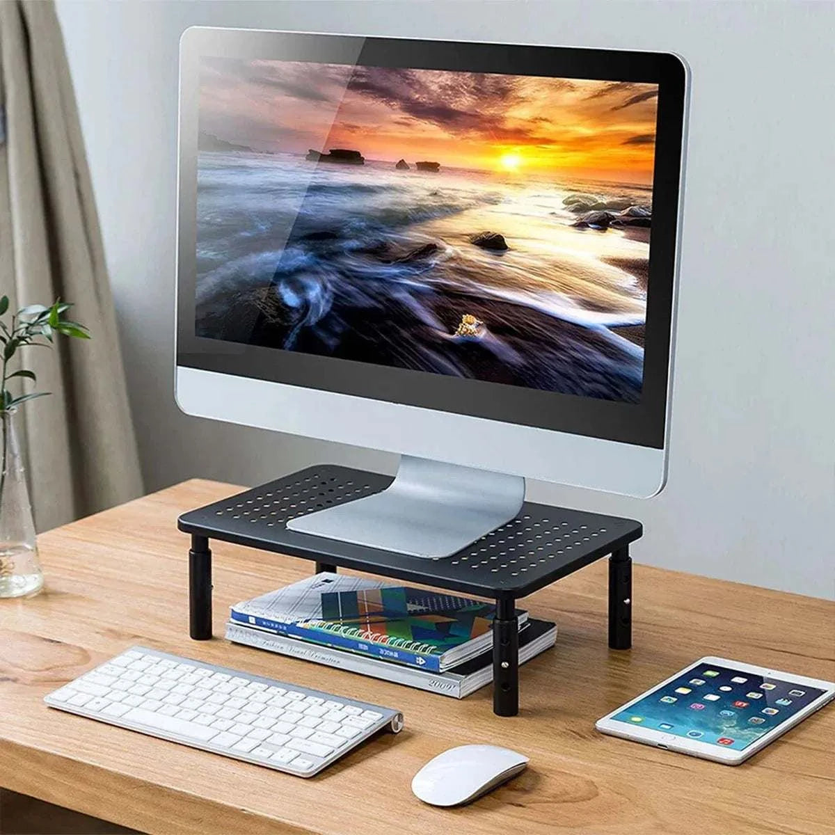 Adjustable Monitor & Laptop Riser in black iron with perforated surface and 3 adjustable height settings supporting a desktop monitor.