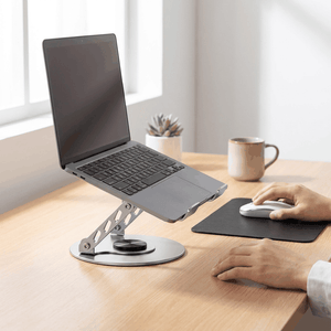 Adjustable aluminum alloy laptop stand in silver with a perforated support arm and round rotating base beneath a laptop