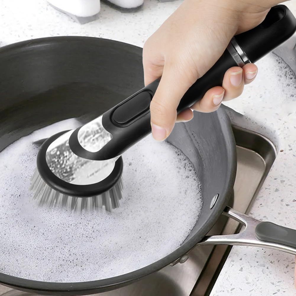 Automatic Liquid Adding dishwashing brush in black with a soap-dispensing handle and grey nylon bristles scrubbing a pan