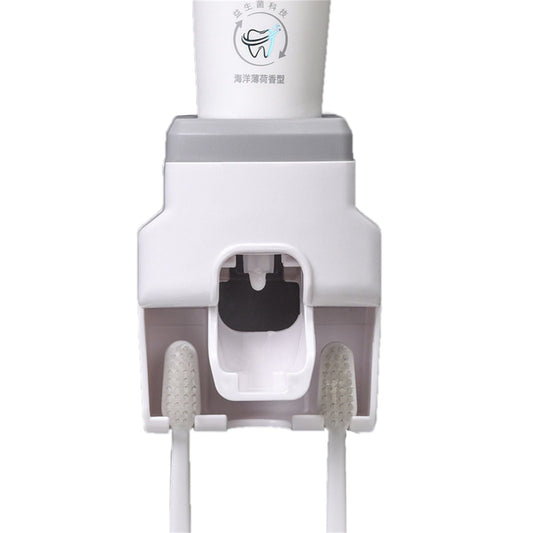 Automatic Toothpaste Dispenser with a white and grey plastic body, central dispensing nozzle and two toothbrush holders