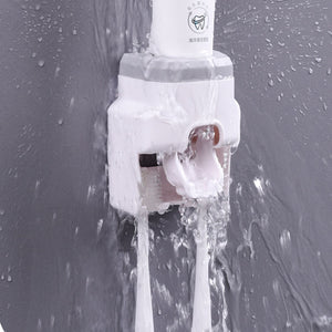 Automatic Toothpaste Dispenser in white plastic with a built-in toothbrush holder, shown releasing toothpaste as water runs over it