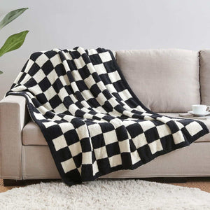 Knitted throw blanket in black and white with a bold checkerboard pattern and soft, plush texture. Black and White Premium Knitted Checkerboard draped over a sofa.