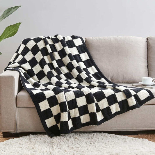 Knitted throw blanket in black and white with a bold checkerboard pattern and soft, plush texture. Black and White Premium Knitted Checkerboard draped over a sofa.