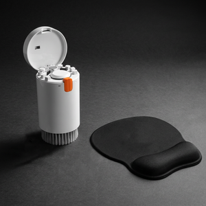 Black silicone wrist rest with a smooth contoured shape and raised cushioned edge, beside an open white cleaning tool case.