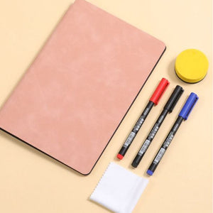 Reusable whiteboard notebook with a smooth pale pink cover and black edging, beside three coloured markers and a yellow eraser; Blue A4 PU Leather