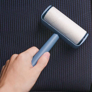 Capsule Sticky Lint Roller with a blue plastic handle and protective shell, showing a white adhesive roll against dark striped fabric.
