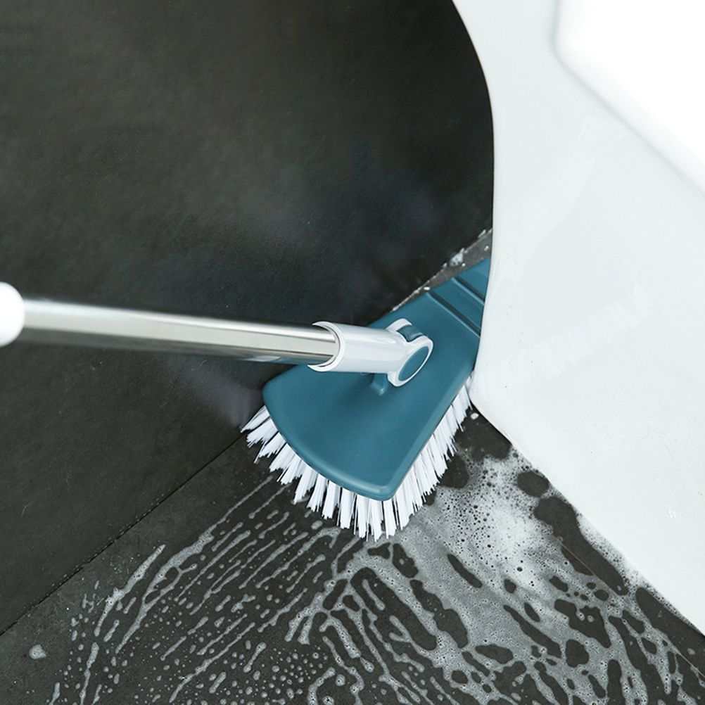 Corner Scrub Brush with a teal plastic angled head, white bristles and a long silver handle scrubbing a tiled corner