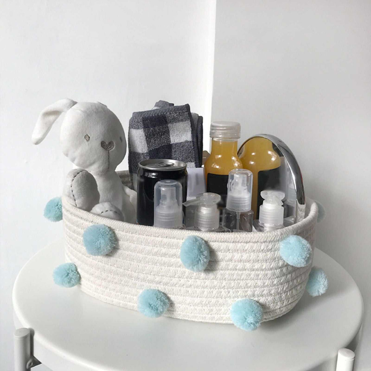 Cotton Rope Knitting storage basket in white woven cotton with pale blue pom-poms, holding toiletries and a plush rabbit