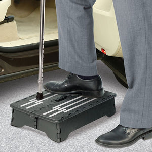 Folding Step Stool in dark plastic with a ridged surface and white anti-slip strips, supporting a person's feet