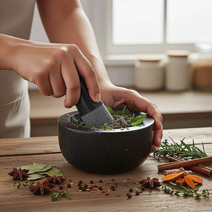 Granite Mortar & Pestle in dark grey speckled stone, with a rounded bowl and matching pestle grinding fresh herbs