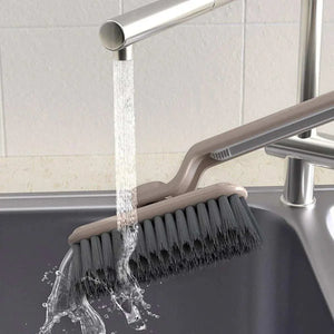 Multifunctional 360° Rotary Cleaning Brush with dark bristles and a curved light-colored handle rinsed under water