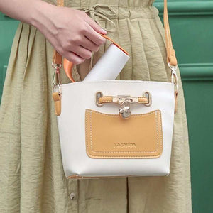 Reusable Lint Roller in orange and white compact plastic design held above a beige and white small handbag with tan accents