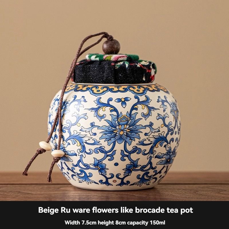 Ru Kiln tea jar in cream ceramic with ornate blue floral motifs, a dark fabric-covered lid and cord tie
