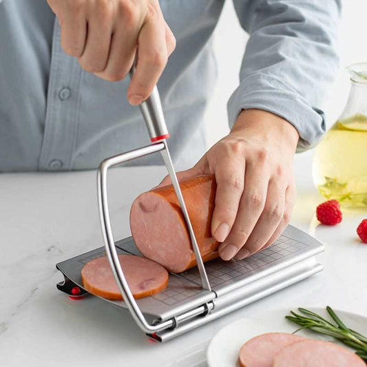 stainless steel cheese slicer with a grey measurement-grid board, metal wire frame and red anti-slip feet slicing ham