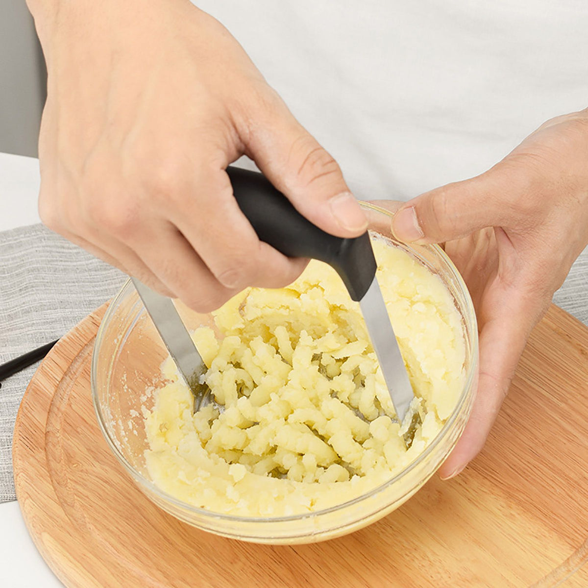 Stainless Steel Potato Masher with black wide-grip handle and twin metal mashing arms pressing cooked potatoes