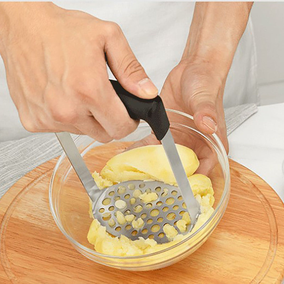 Stainless Steel Potato Masher with a perforated metal plate and black wide-grip handle mashing potatoes