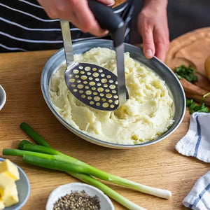Stainless Steel Potato Masher with a perforated metal plate and black wide grip, pressing creamy mashed potatoes