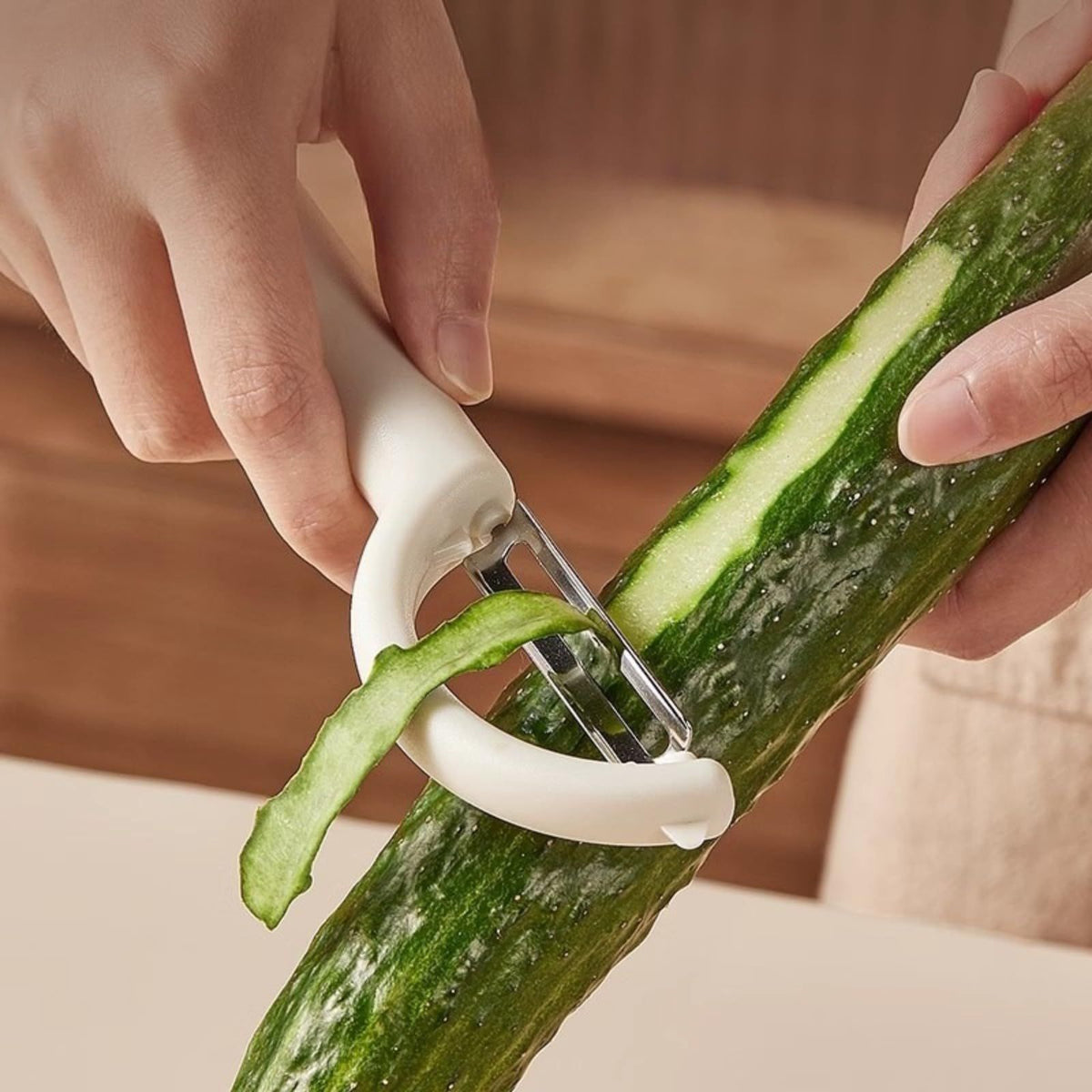 Swivel Vegetable Peeler with a white ergonomic handle and stainless steel blade peeling a dark green cucumber