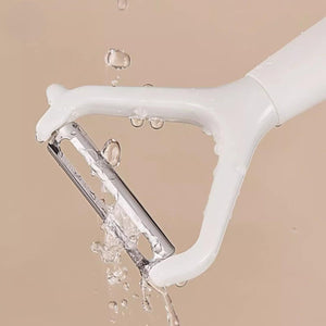 Swivel Vegetable Peeler with a white plastic frame and exposed stainless steel blade, shown with water droplets