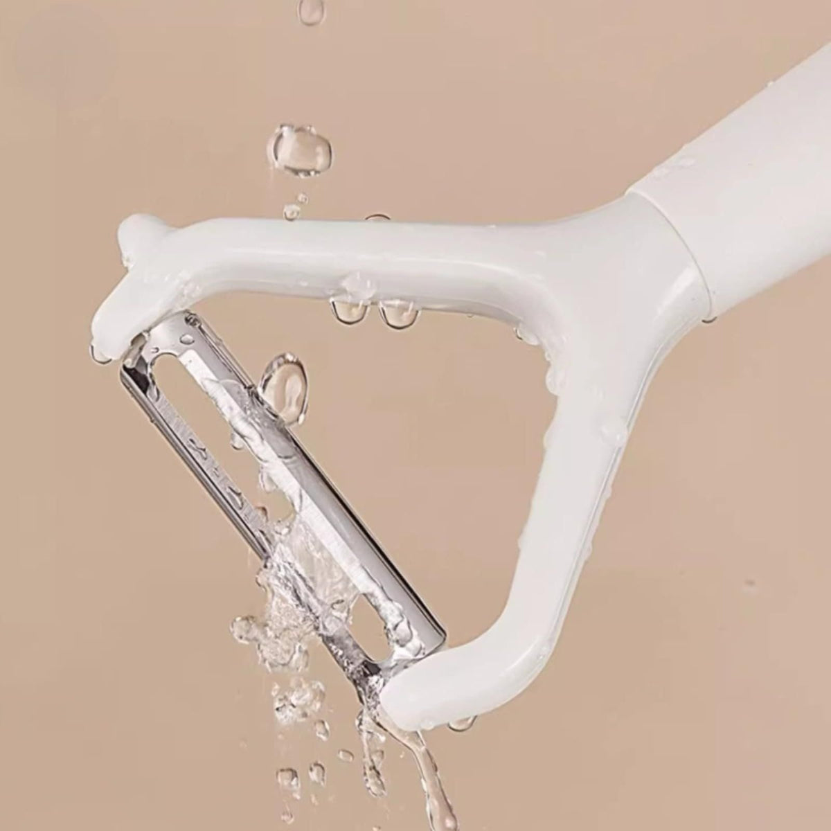 Swivel Vegetable Peeler with a white plastic frame and exposed stainless steel blade, shown with water droplets