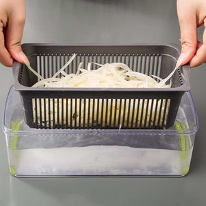 Vegetable Chopper with gray slotted draining basket nested in a clear container, holding thin white vegetable strips
